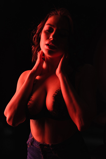 красное освещение на соблазнительную женщину в кружеве бюстгальтер изолирован на черный  - Фото, изображение