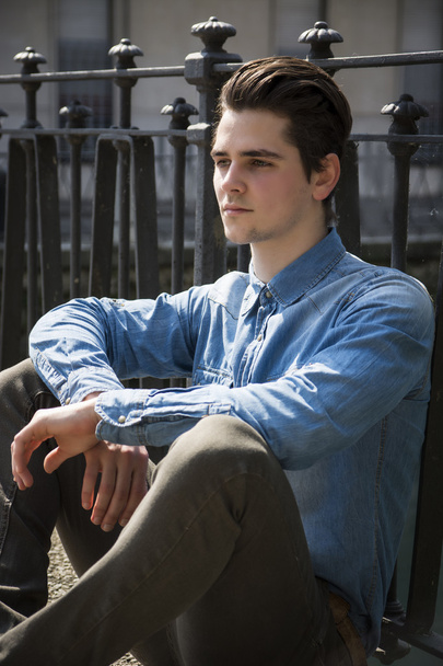Handsome young man sitting against handrail outdoors - Фото, изображение