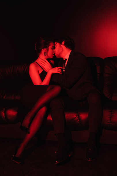 Siyah deri koltukta öpüşen seksi çifte kırmızı ışık.  - Fotoğraf, Görsel