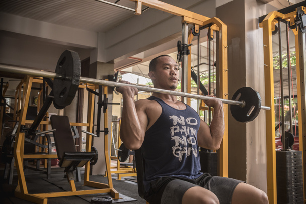 Ein athletischer und robuster asiatischer Mann macht sitzende Militärpressen. Schultertraining im Fitnessstudio. - Foto, Bild