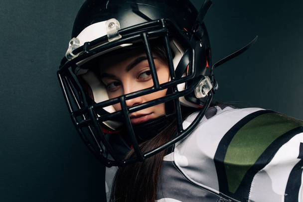 Portrait of beautiful sexy young woman on black background in American football uniform and helmet. - Photo, Image