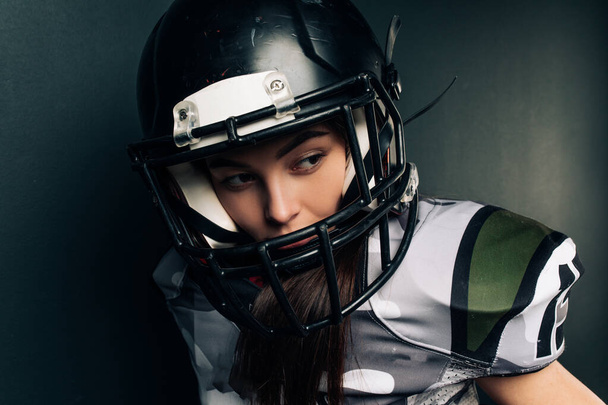 Porträt der schönen sexy jungen Frau auf schwarzem Hintergrund in American-Football-Uniform und Helm. - Foto, Bild