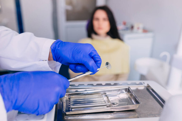 Руки дантиста в синих перчатках работают с зубными инструментами. пациент сидит в стоматологическом кресле на заднем плане. - Фото, изображение