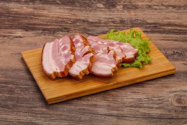 Вкусная копченая свиная грудинка на деревянной доске - Фото, изображение