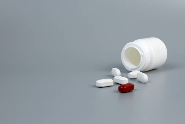 Biały słoik z rozrzuconymi tabletkami na szarym tle - Zdjęcie, obraz