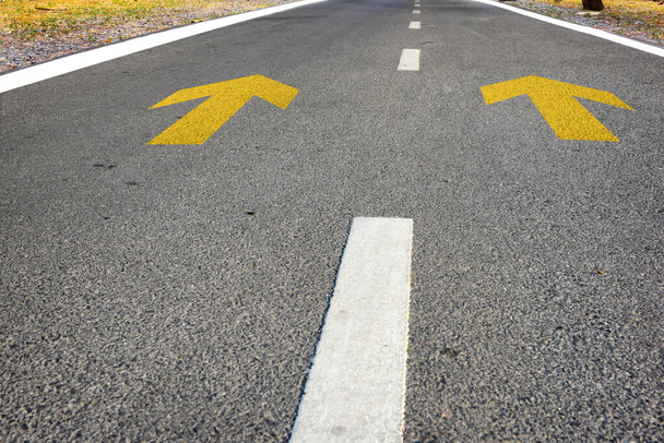 Segnale freccia gialla marcatura sul manto stradale nel parco per dare indicazioni. Concetto di trasporto e idea di viaggio su strada - Foto, immagini