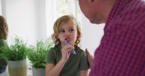 Caucasian grandfather helping his grandson to brush his teeth at home. family, togetherness and happiness concept - Filmati, video