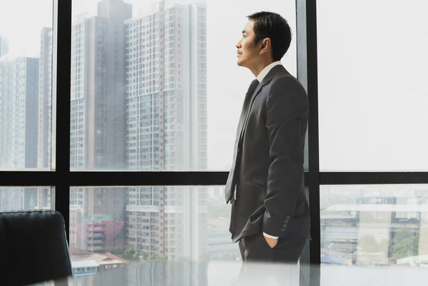 Επιχειρηματίας στέκεται δίπλα στο παράθυρο κοιτάζοντας έξω από την πλαϊνή όψη. - Φωτογραφία, εικόνα