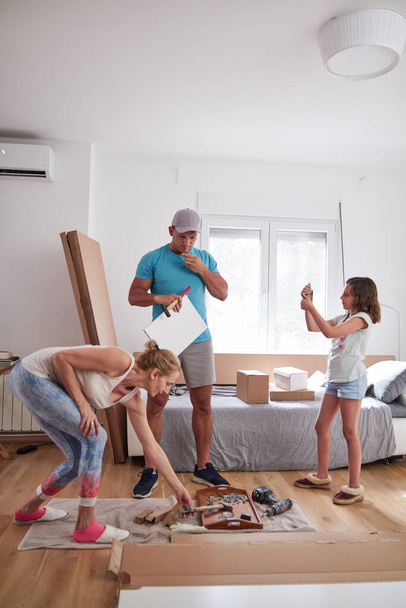 Mère, père et fille assemblant des meubles dans un nouvel appartement, emménageant et travaillant dur. - Photo, image