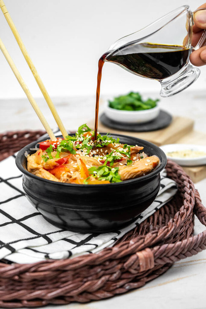 Ensalada asiática con fideos de arroz, verduras, champiñones, pollo y salsa de soja. Funchose con fideos blancos transparentes en placa negra - Foto, Imagen