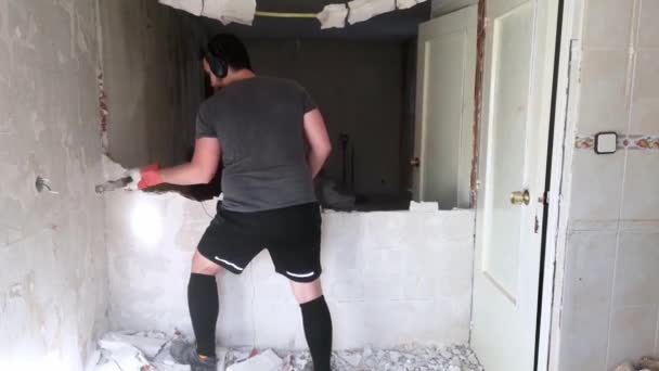 Een jongeman die een muur breekt met een hamer. Huisrenovatie. - Video