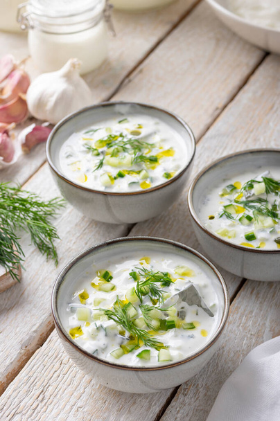 Традиційний літній холодний суп з домашнього йогурту, огірків та свіжих трав на дерев'яному столі
 - Фото, зображення