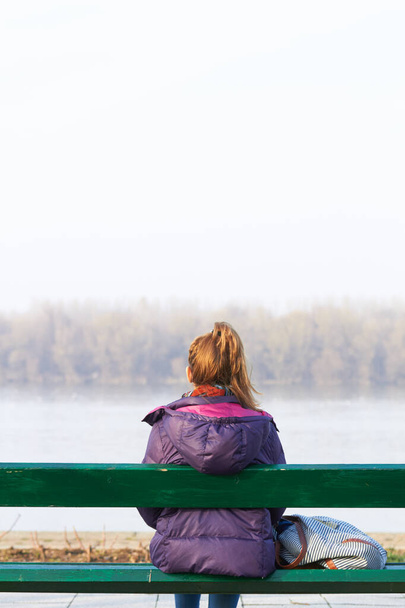 Chica solitaria sentada en un banco y mirando a la distancia. - Foto, Imagen