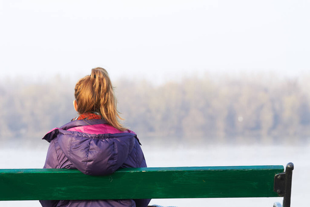 Chica solitaria sentada en un banco y mirando a la distancia. - Foto, imagen
