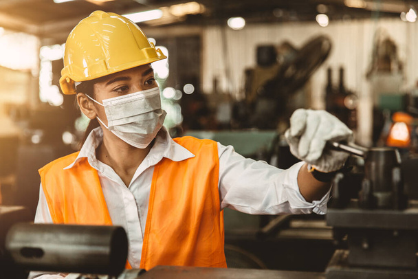 aziatische vrouw werknemer met veiligheid helm en gezicht masker werken als arbeider in zware industrie fabriek. - Foto, afbeelding