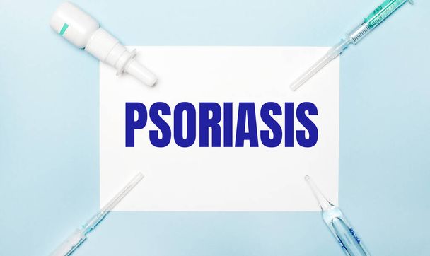 On a light blue background, syringes, a medicine bottle, an ampoule and a white sheet of paper with the text PSORIASIS. Medical concept. - 写真・画像