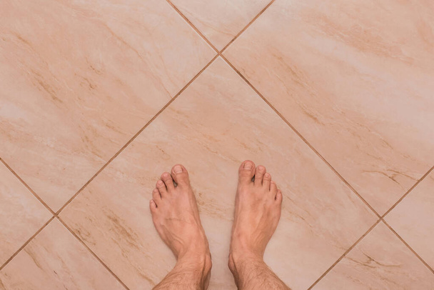 Mezítlábas férfi láb áll a könnyű kerámia csempe padló háttér, kilátás felülről. - Fotó, kép