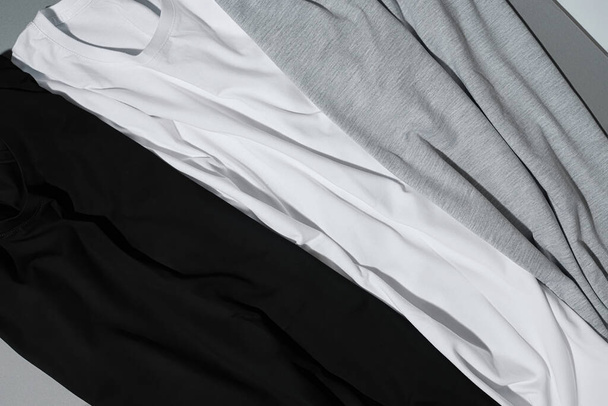 Primer plano de tres camisetas de algodón monocromo se burlan de fondo gris - Foto, imagen