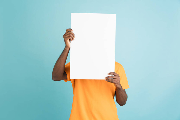 Young African man with blank sheet of paper isolated over blue studio background. - Foto, Imagen