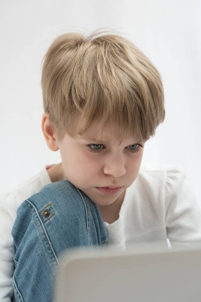 The blond child looks attentively at the computer or laptop screen. Close-up portrait - Fotoğraf, Görsel