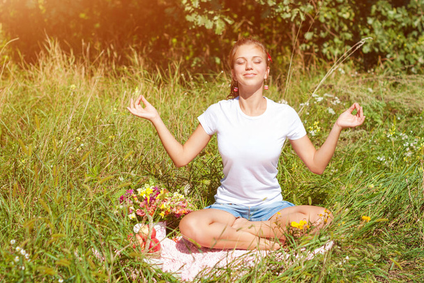 Jonge vrouw mediterend in lotuspositie terwijl ze yoga doet in een prachtig bos. Reizen, gezonde levensstijl concept. - Foto, afbeelding