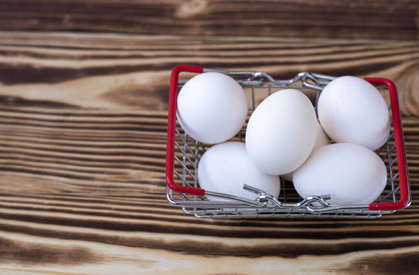 weiße Hühnereier in einem Lebensmittelkorb stehen auf einem verbrannten Holzgrund.  - Foto, Bild