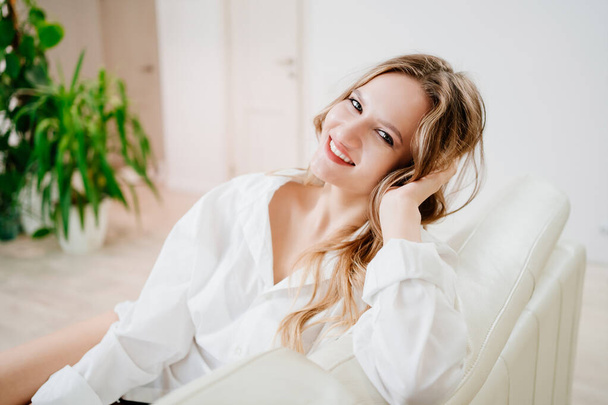 portrait of a beautiful young woman in a white shirt on the sofa in a white room - Foto, Imagen