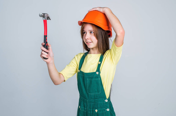 teen girl laborer in protective helmet and uniform on grey background use hammer, worker - Photo, Image
