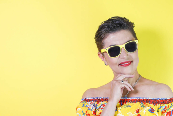 A Hispanic female with sunglasses posing against a yellow wall - copy space - Φωτογραφία, εικόνα