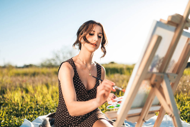 Retrato de beleza jovem pintura sobre tela no campo de flores ao pôr do sol  - Foto, Imagem