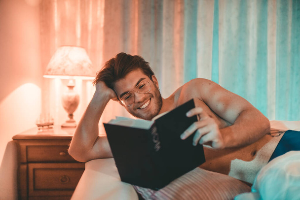 Portrait of young man reading book in bad at home interior  - Foto, Imagem