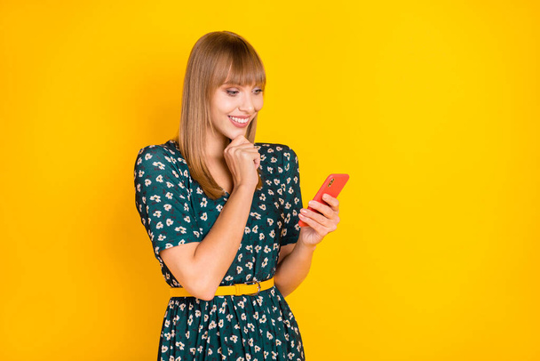 Portrait of attractive focused cheerful blonde girl using gadget browsing media app isolated over bright yellow color background - Foto, imagen