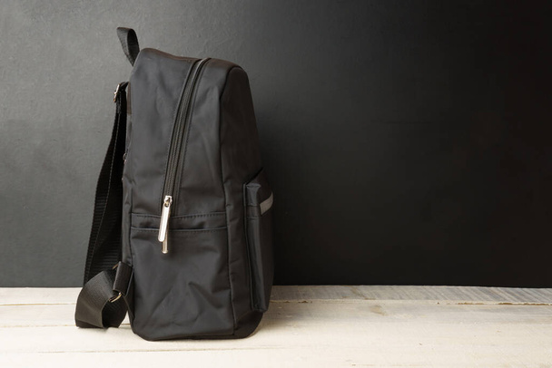 backpack on a black wall background, on a white wooden table with copy space - Fotoğraf, Görsel