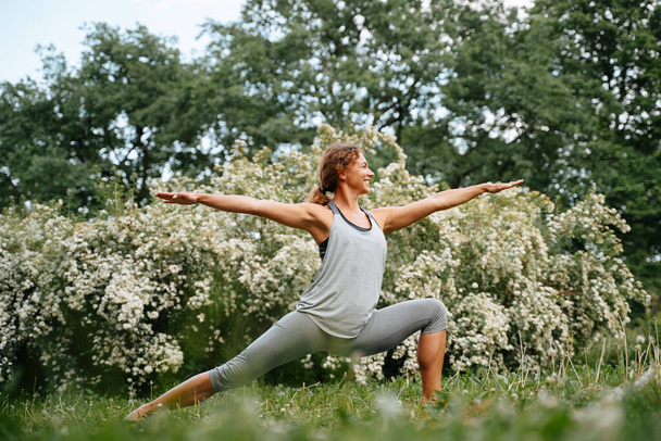 Young sportive woman practices yoga in park - 写真・画像