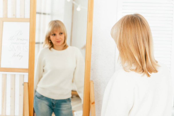 vrouw staan in de buurt van spiegel en kijken naar reflectie - Foto, afbeelding
