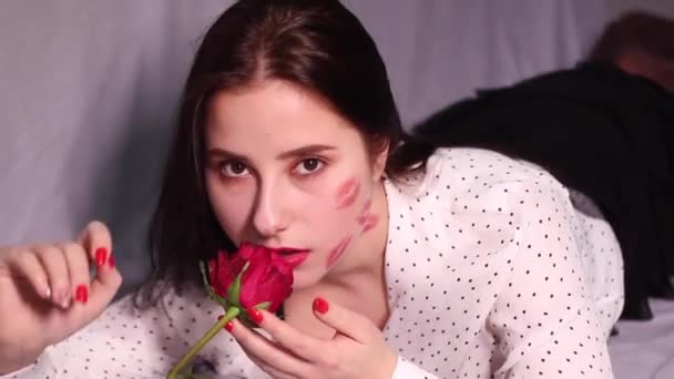 sexy brunette vrouw met kussen, lippenstift markeringen op haar gezicht en nek, met rode roos. vriendin, afspraakje, relatieperiode. kopieerruimte - Video