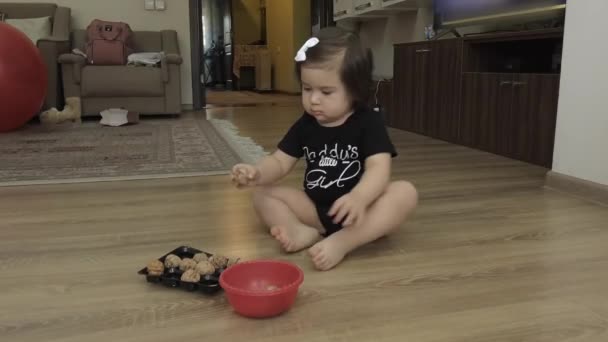 The child sits on the floor in the room and transfers the nuts from the cup to the mold. Having shifted everything, she claps her hands happily. - Footage, Video