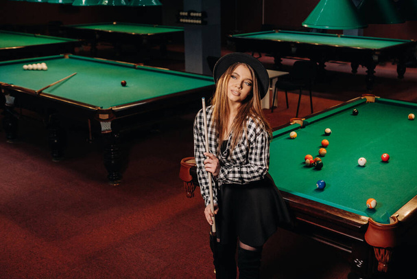 A girl in a hat in a billiard club with a cue in her hands.billiards Game. - Foto, Imagen
