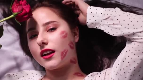 sexy brunette vrouw met kussen, lippenstift markeringen op haar gezicht en nek, met rode roos. vriendin, afspraakje, relatieperiode. kopieerruimte - Video