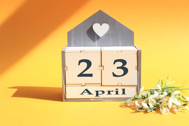 Calendar for April 23 : cubes with the numbers 0 and 22, the name of the month of April in English, a bouquet of blooming snowdrops on a yellow background in the sun and in the shade of objects - Photo, image