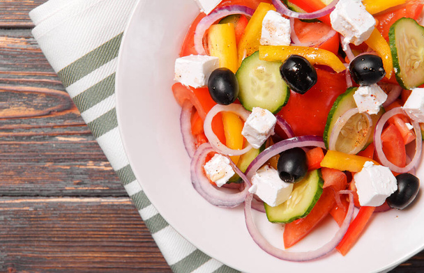 greek vegetable salad with feta tomatoes cucumber and olives in a white plate on a towel on a wooden background top view - Fotoğraf, Görsel