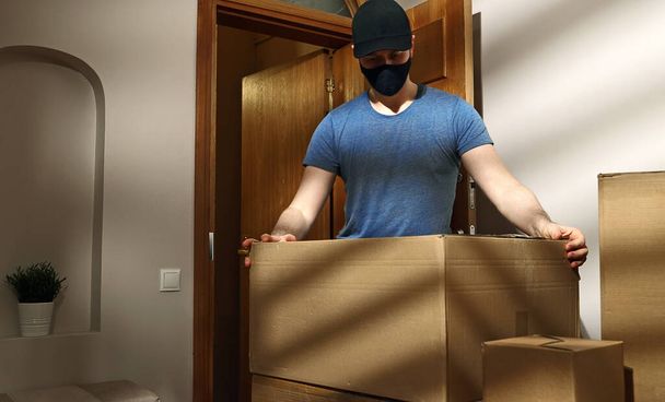 Человек в маске в кепке доставляет картонные коробки. - Фото, изображение