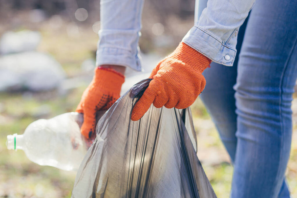 公園や森でゴミを拾うボランティアの男を閉じます。エココンセプト、女性の手はゴミ袋にペットボトルを入れ - 写真・画像