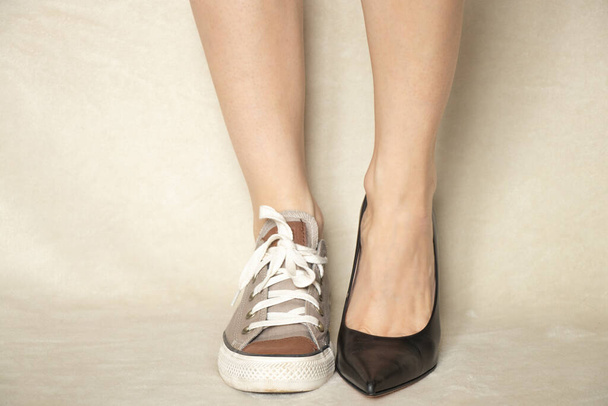 Sport-Sneaker und klassische High Heels schwarz an den Füßen des Mädchens, die Wahl der Schuhe, was zu tragen ist - Foto, Bild
