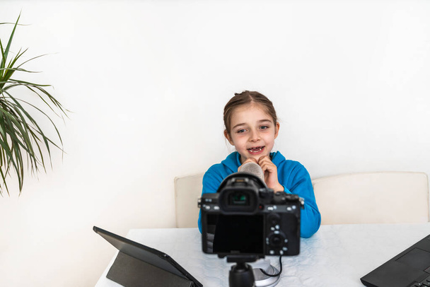 fiatal lány befolyásoló és blogger élő közvetítés a nappaliból nevetés és szórakozás nézi a kamerát, és beszél a mikrofonba egy video platform vagy a szociális hálózat - Fotó, kép