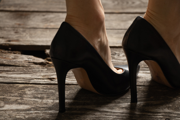 female feet in black leather high-heeled shoes on old wooden floor, womens shoes - Photo, Image