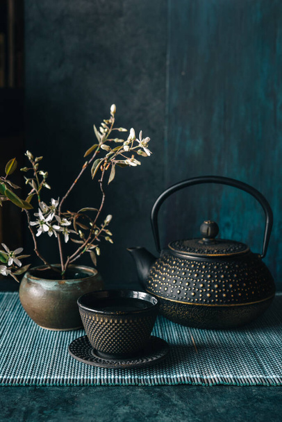 Black iron Asian teapot with cup of tea, wabi-sabi pot with spring flower - Photo, Image