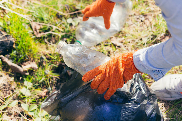 close up Volunteer man picking up trash in the park and forest. Ecology concept, female hand puts a plastic bottle in a garbage bag - 写真・画像