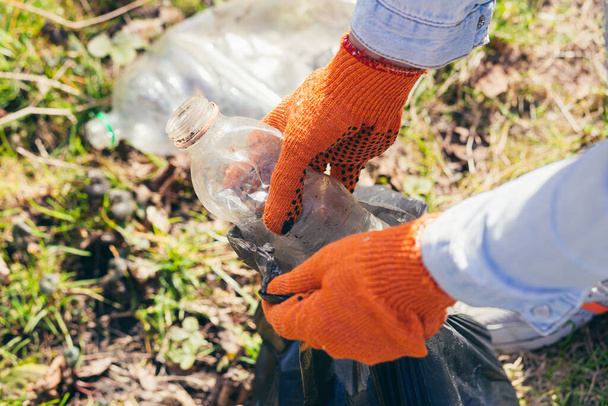 close up Volunteer man picking up trash in the park and forest. Ecology concept, female hand puts a plastic bottle in a garbage bag - Fotó, kép