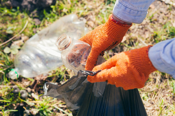 close up Volunteer man picking up trash in the park and forest. Ecology concept, female hand puts a plastic bottle in a garbage bag - 写真・画像